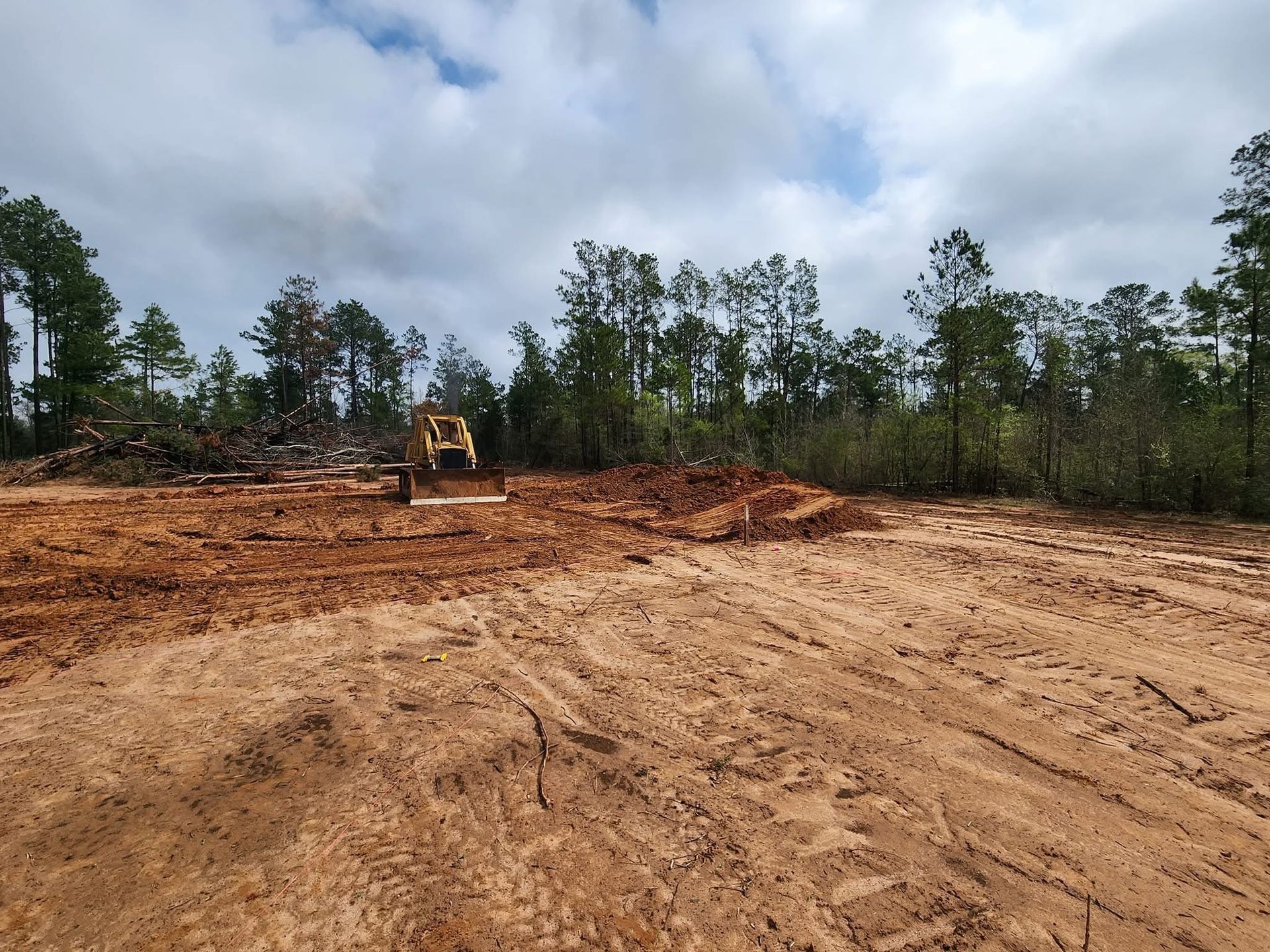 Bulldozer clearing dirt on a construction site with trees in the background under a cloudy sky.