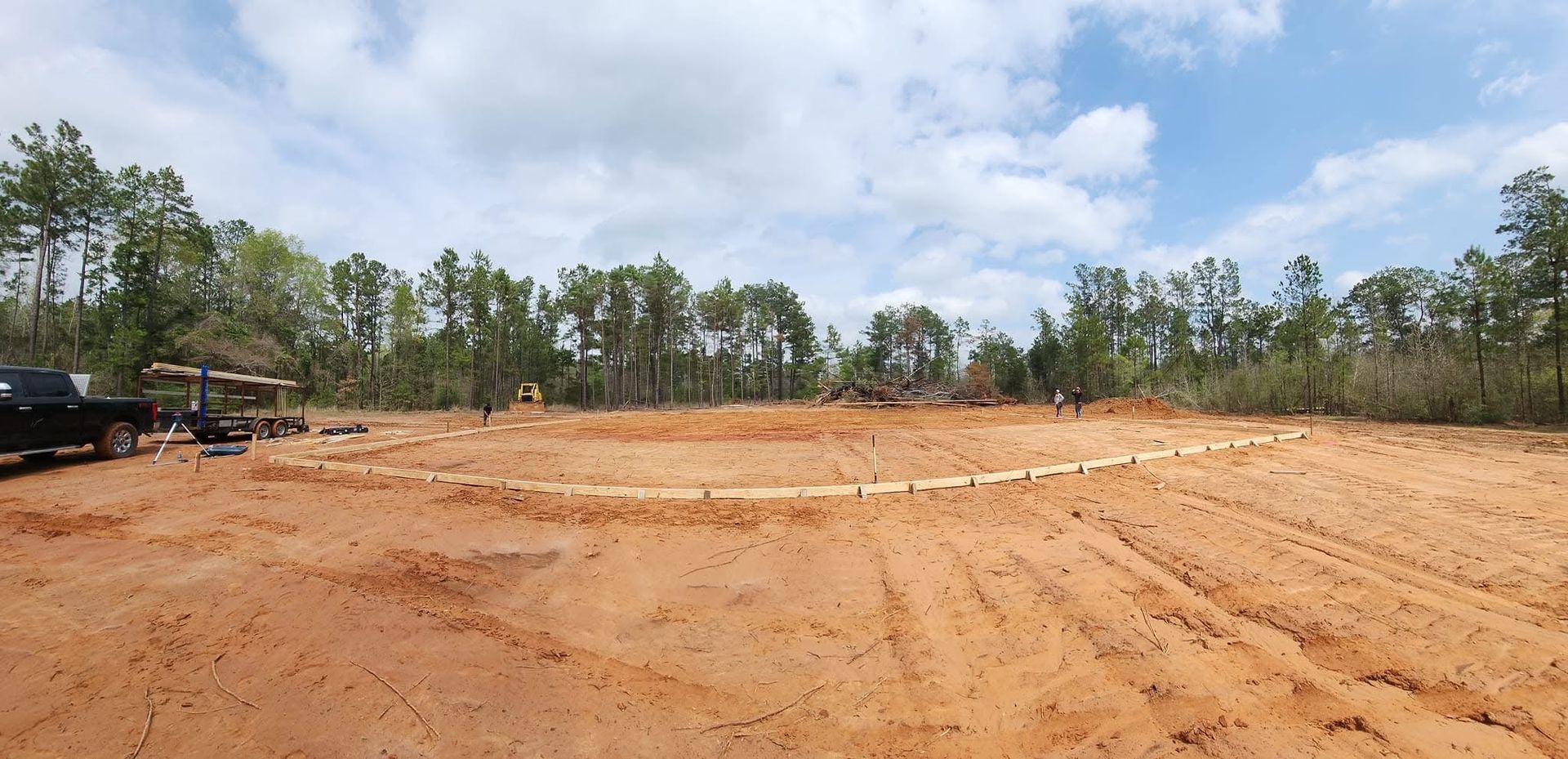 Dirt clearing on a sunny day, with trees in the background. A truck sits on the left.