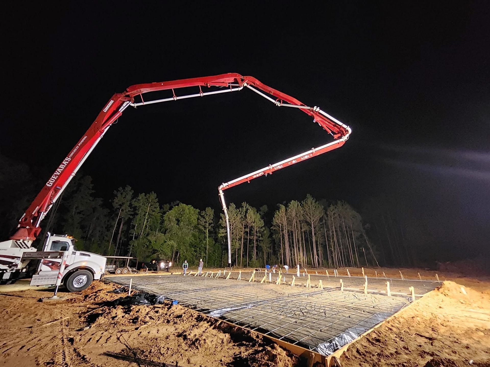 Concrete pump truck pouring concrete on a prepared foundation at night.
