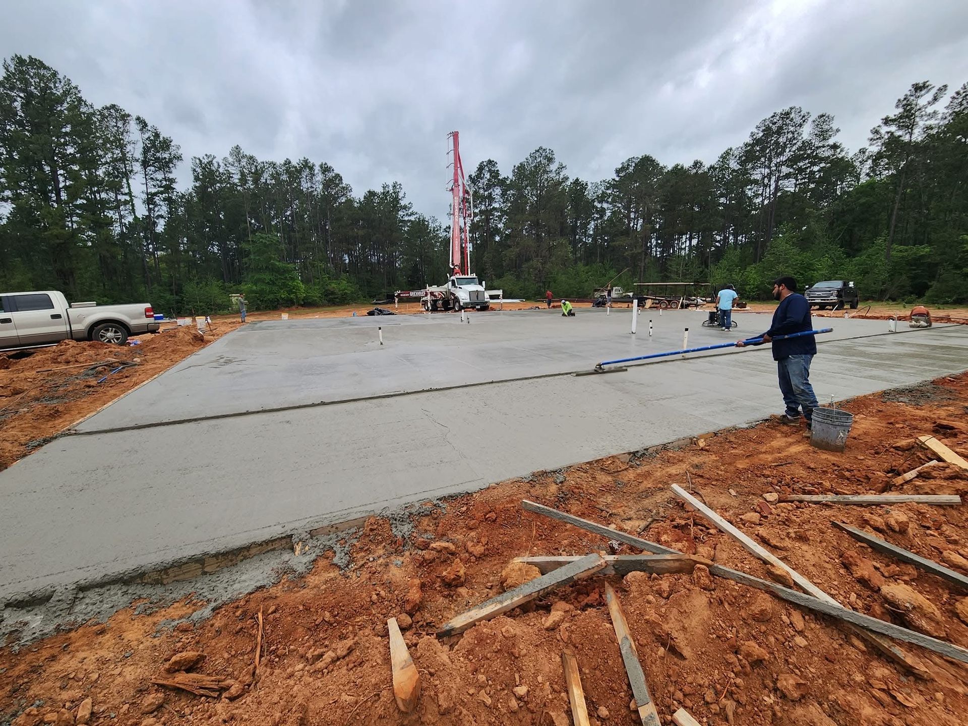 Concrete slab being poured on a construction site; workers leveling the wet concrete, truck with pump.