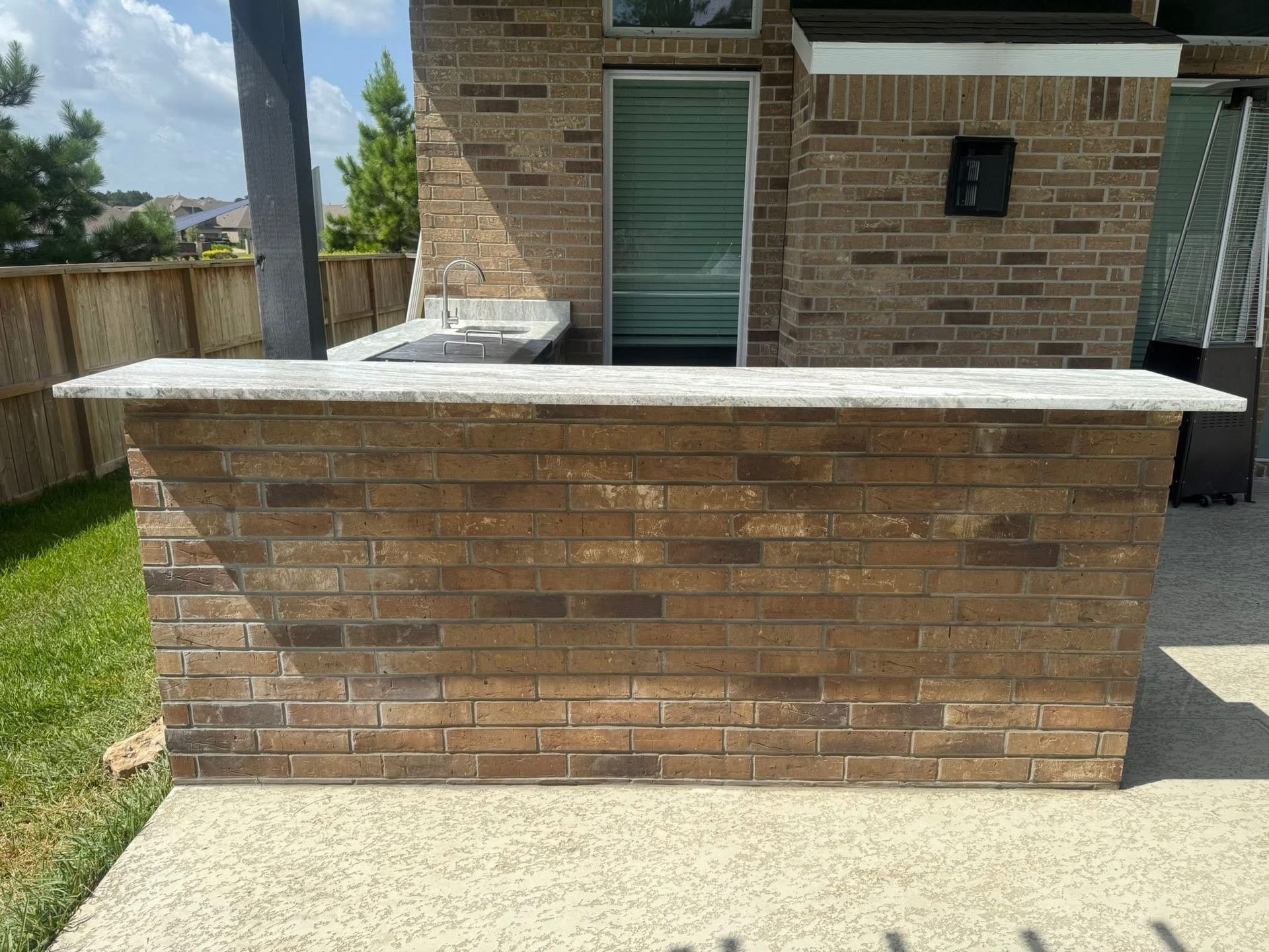 Outdoor brick bar with light-colored countertop; built-in grill in the background. Sunny day.