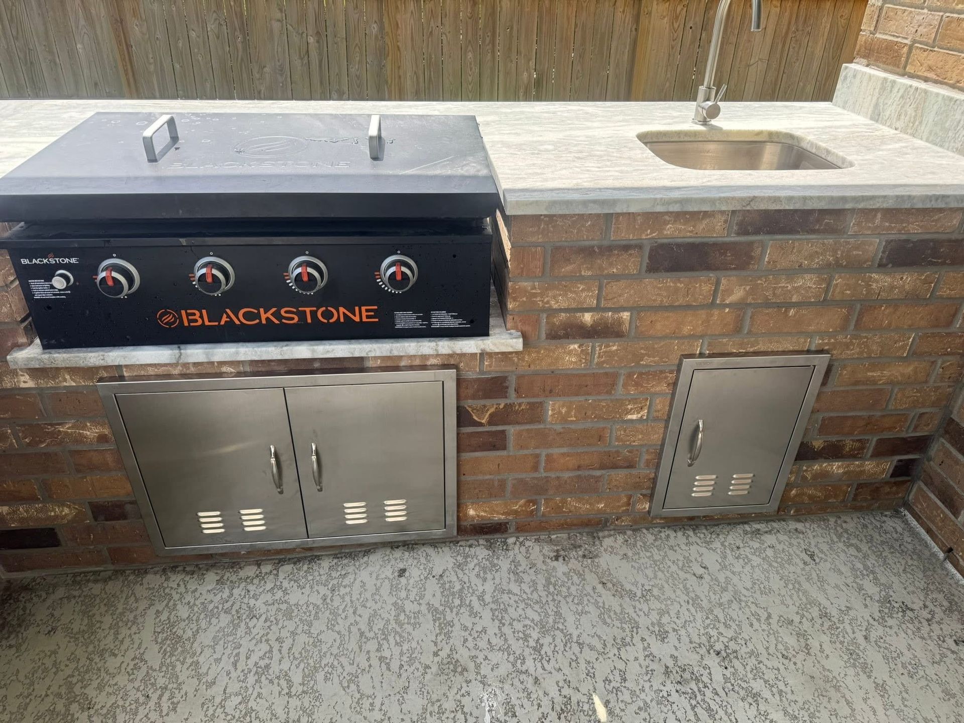 Outdoor kitchen with brick base, Blackstone griddle, sink, and stainless steel storage.