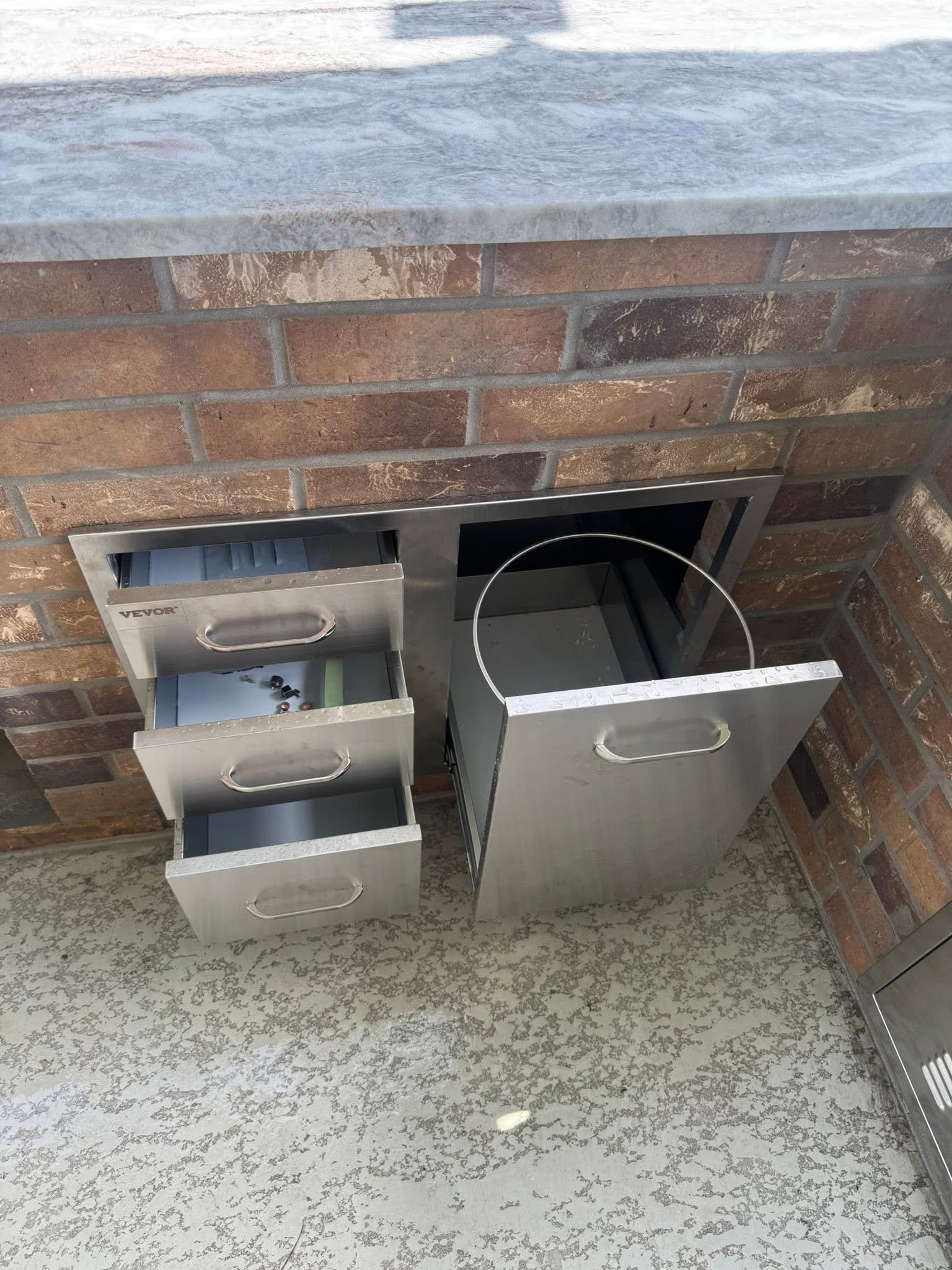 Stainless steel drawers built into a brick structure, one drawer open.