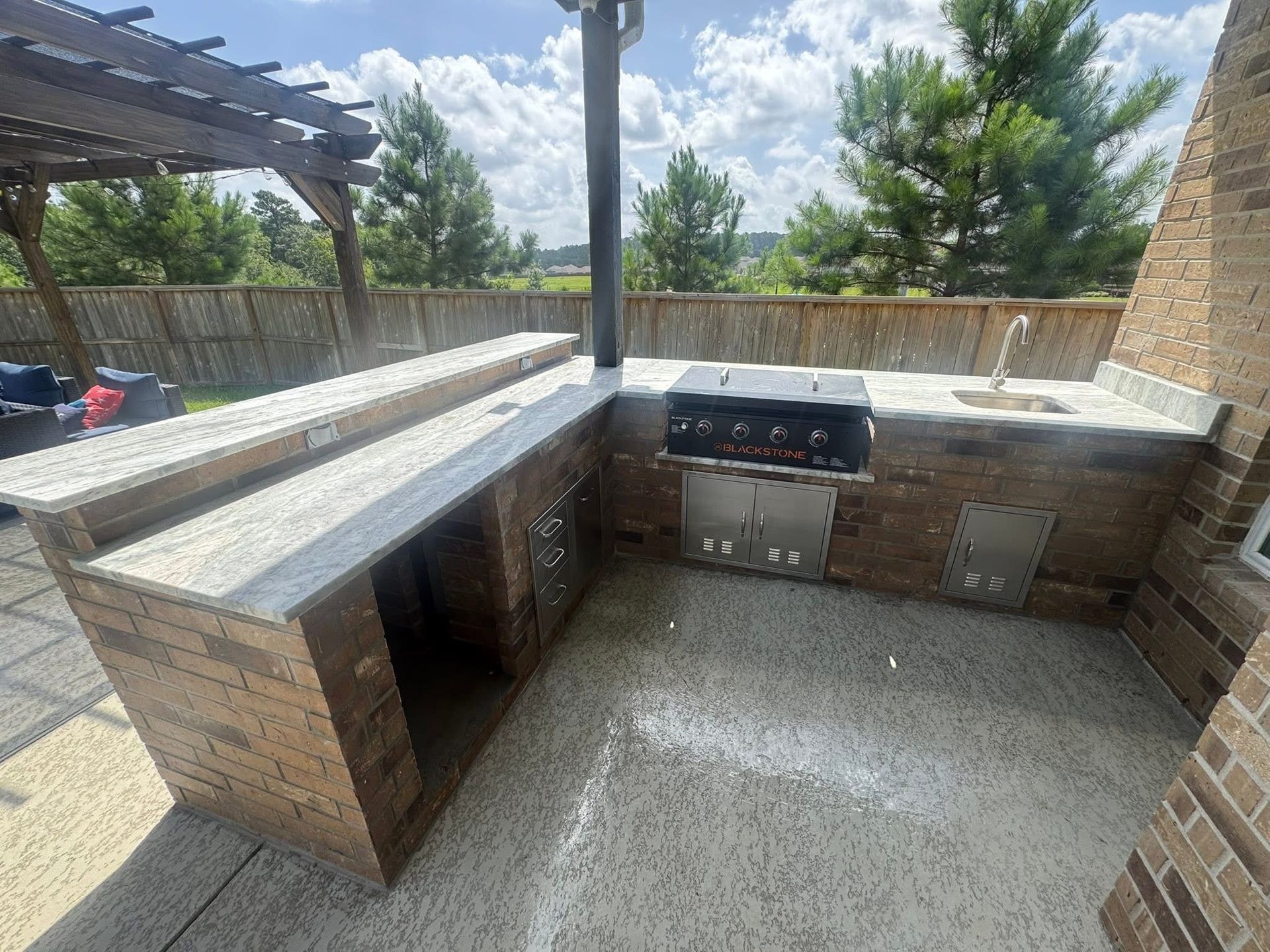 Outdoor brick kitchen with grill, sink, and countertops. Sunny day.