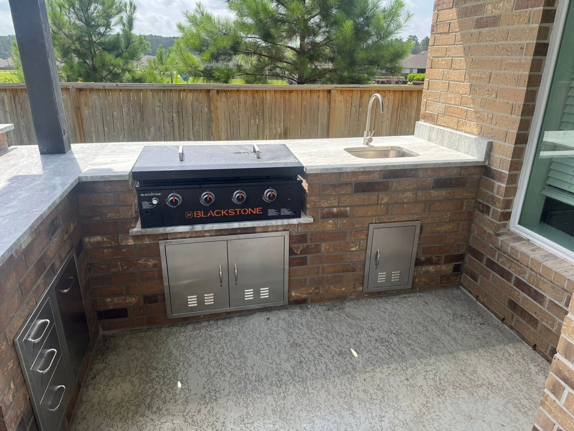 Outdoor kitchen with a grill, sink, and storage cabinets built into brick.