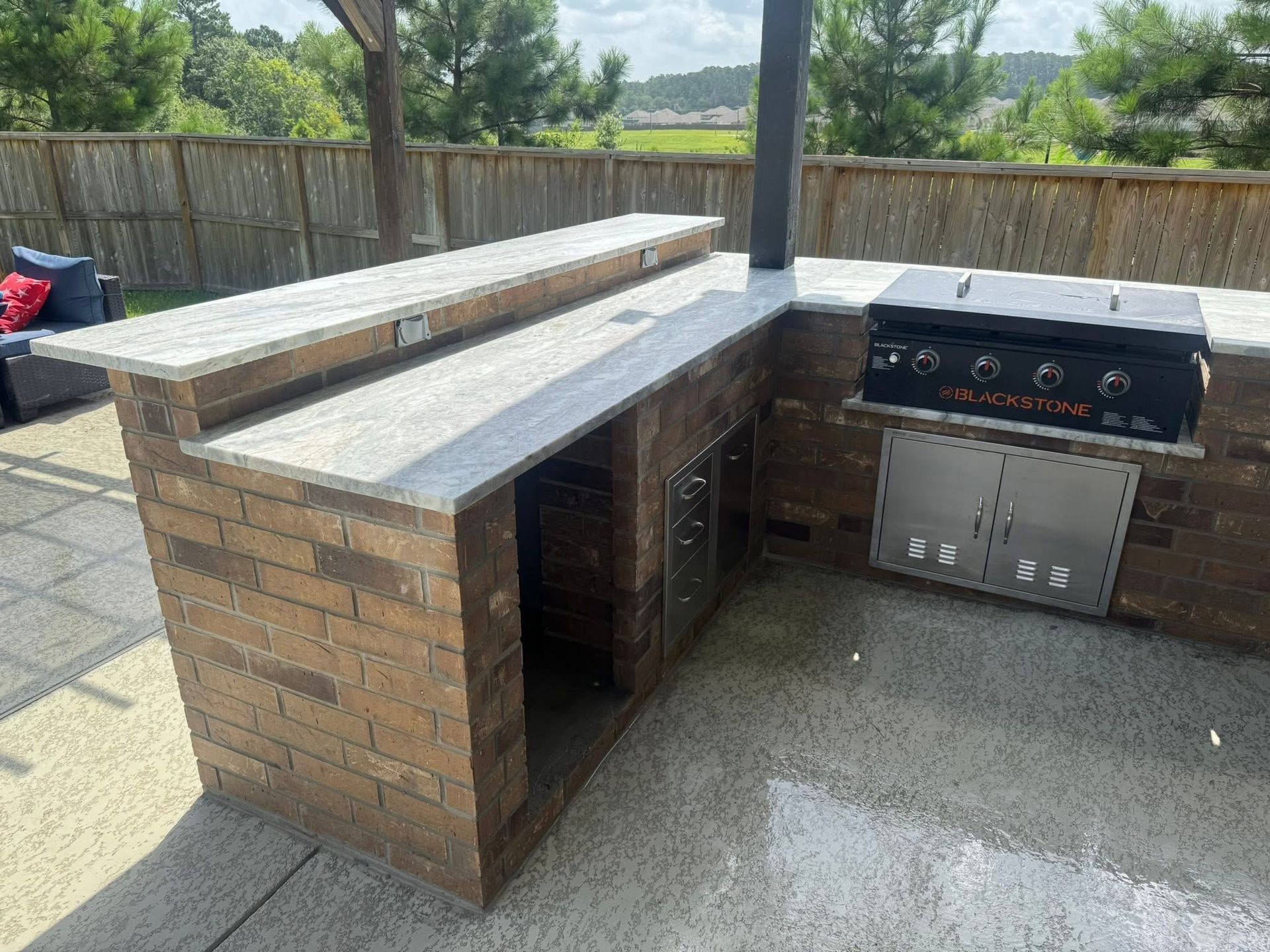 Outdoor kitchen with brown brick, granite countertop, stainless steel grill, and bar.
