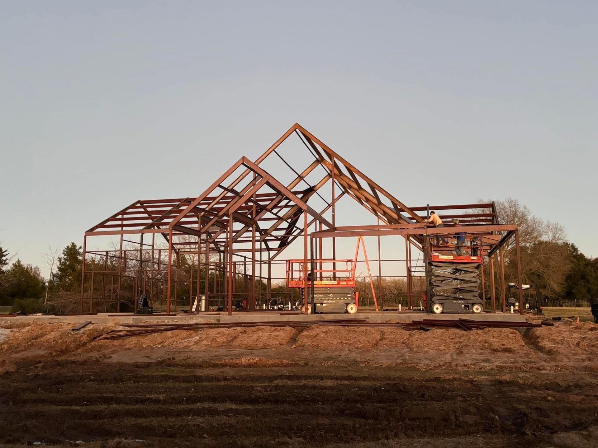 Steel frame of a building under construction on a dirt lot; daylight.
