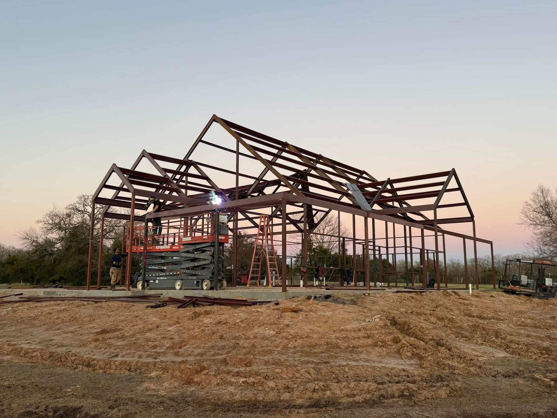 Steel frame of a building under construction against a twilight sky. Brown metal beams, brown field.