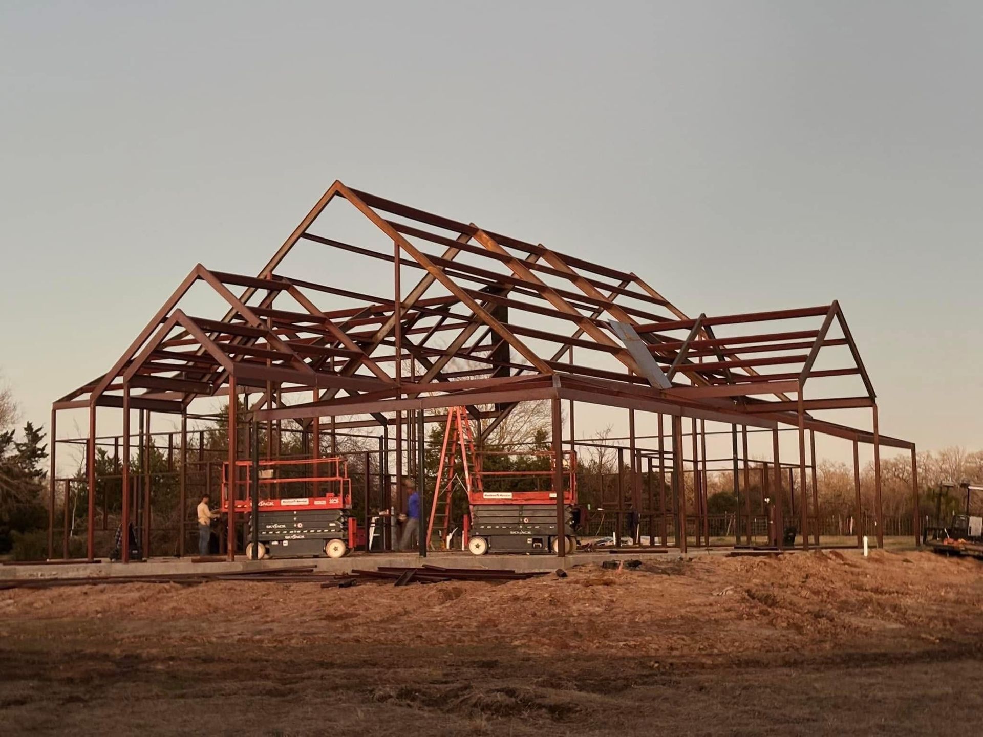 Steel frame of a building under construction, outdoors. Workers on lifts, clear sky.