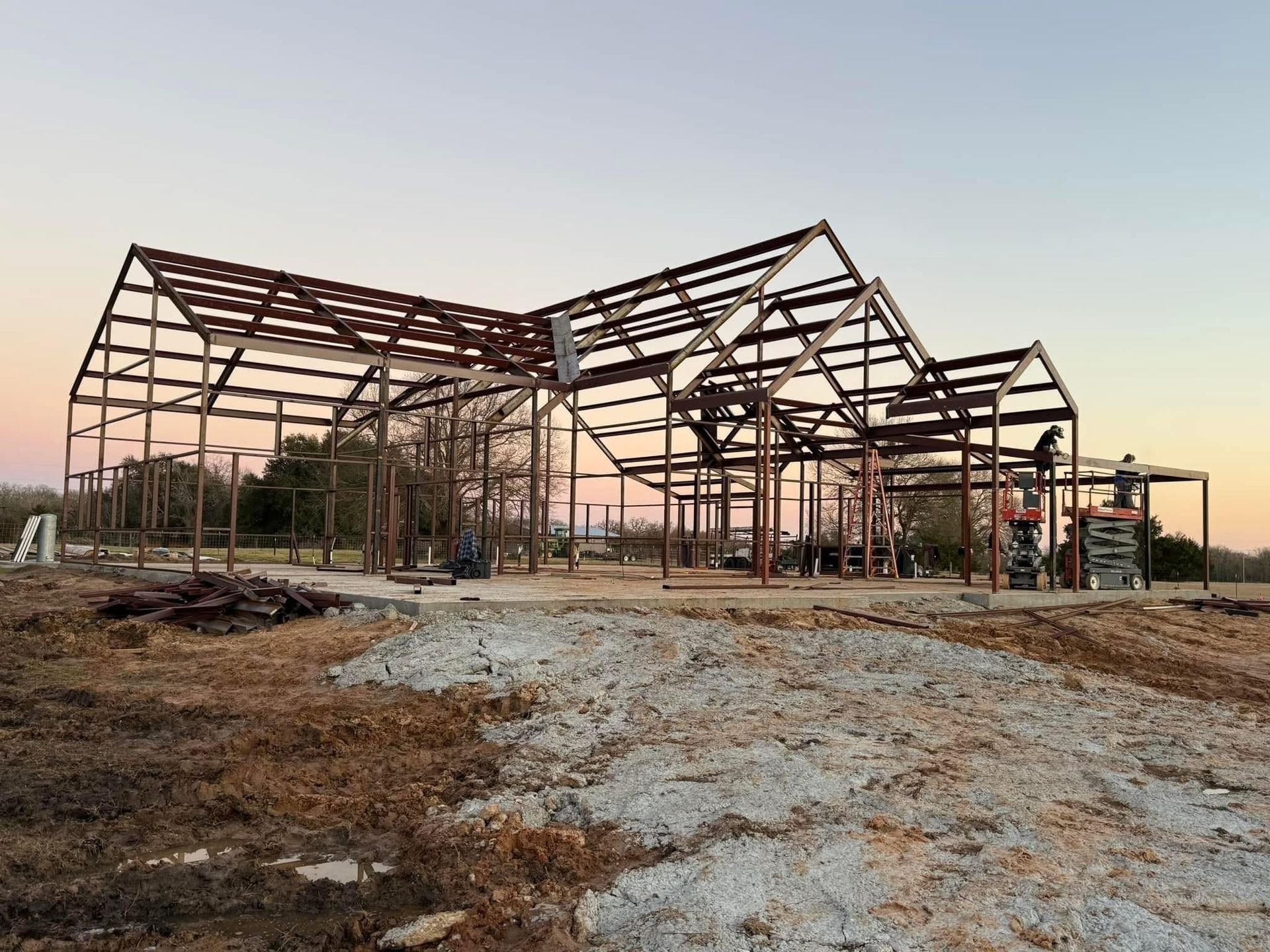 Metal frame of a building under construction at dusk. Brown steel beams, open sky.
