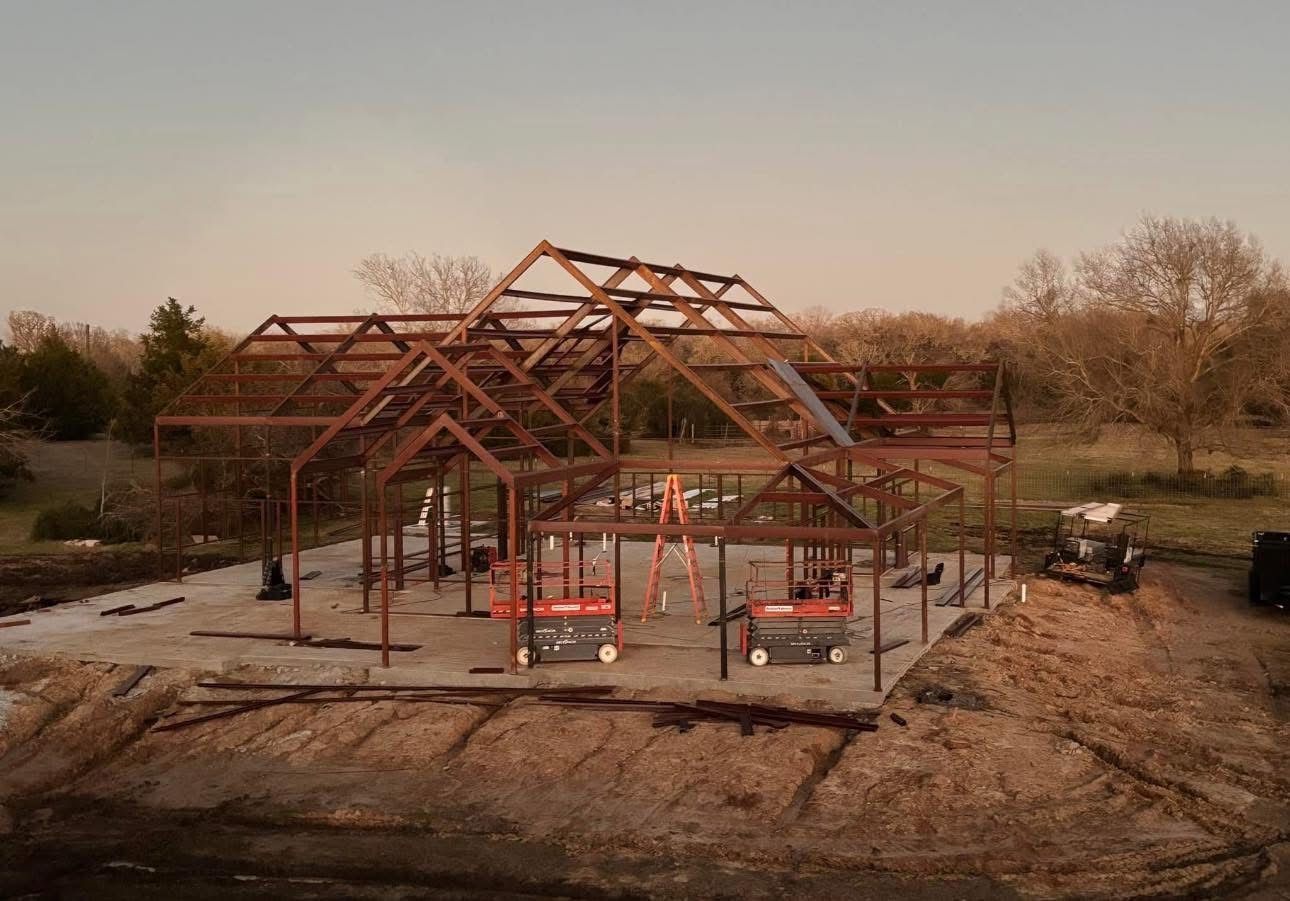 Steel frame of a house under construction, set on a concrete foundation, outdoors.