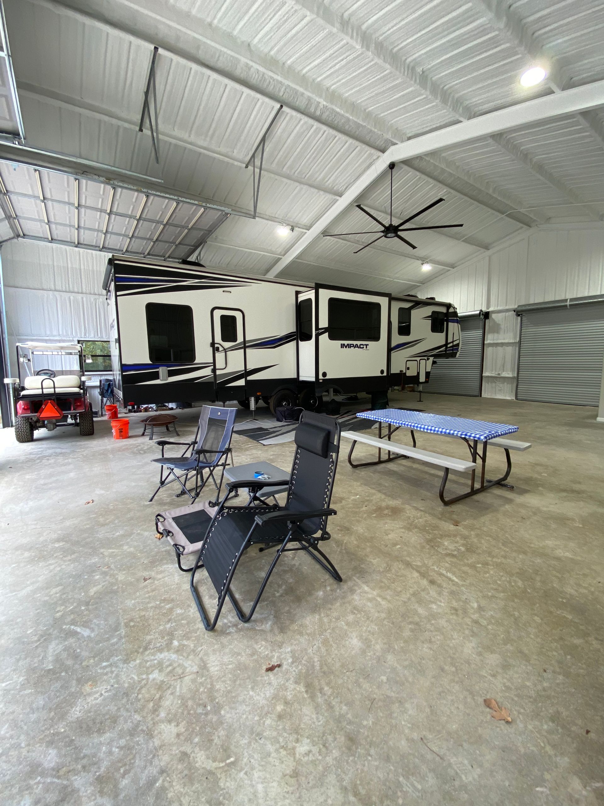 RV parked inside a large, bright metal building with chairs and picnic table.