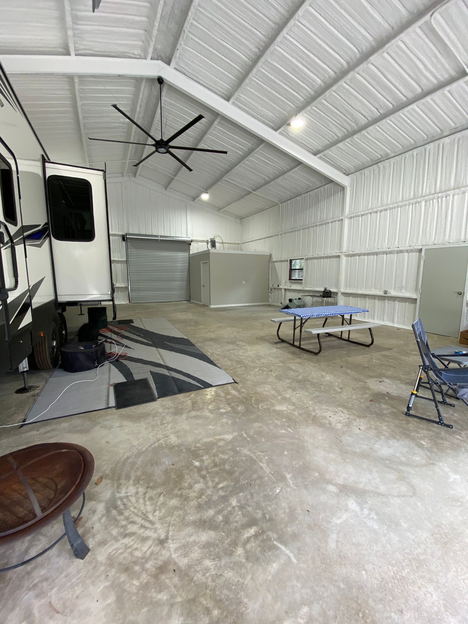 RV under a white metal carport with a table, chairs, and fire pit.
