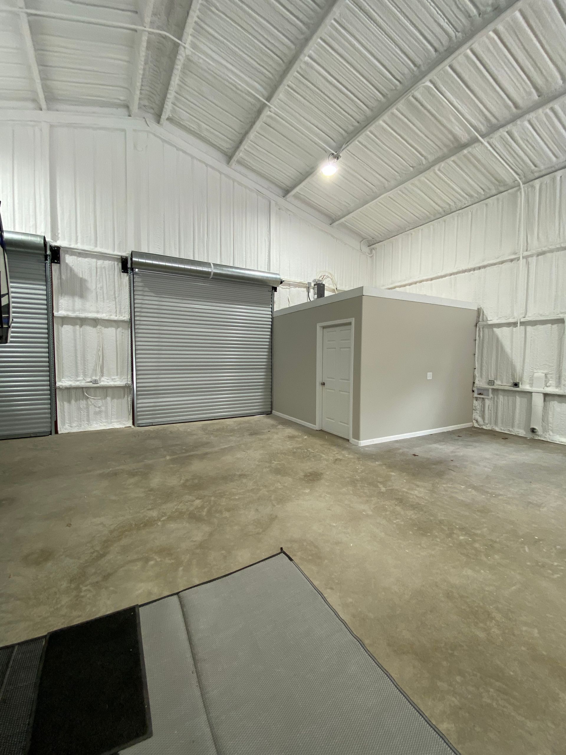 Empty, spacious white warehouse interior with a gray concrete floor, a storage room, and a closed roller door.