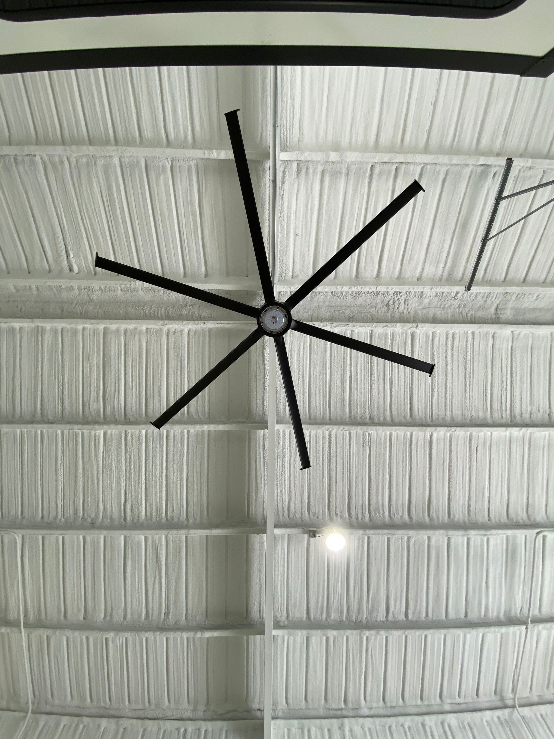 Black ceiling fan on a white foam ceiling with vertical beams, and a single overhead light.