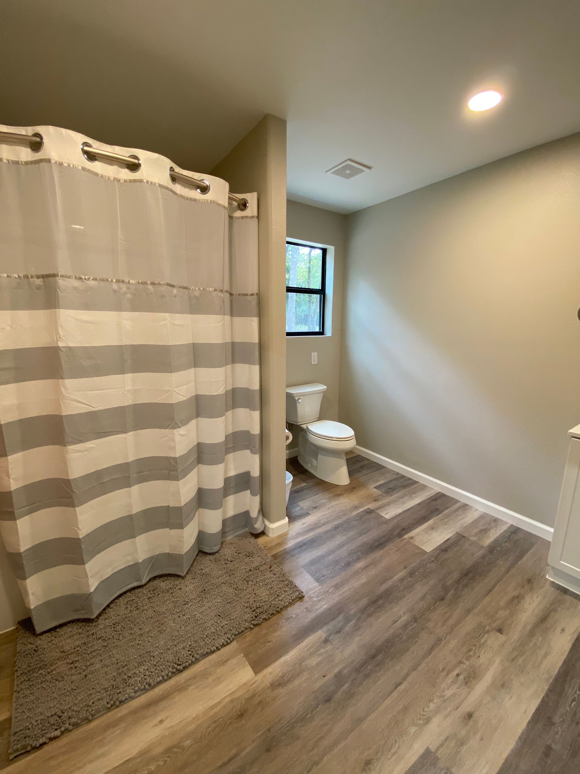 Bathroom with gray and white striped shower curtain, toilet, wood-look flooring, and neutral-colored walls.