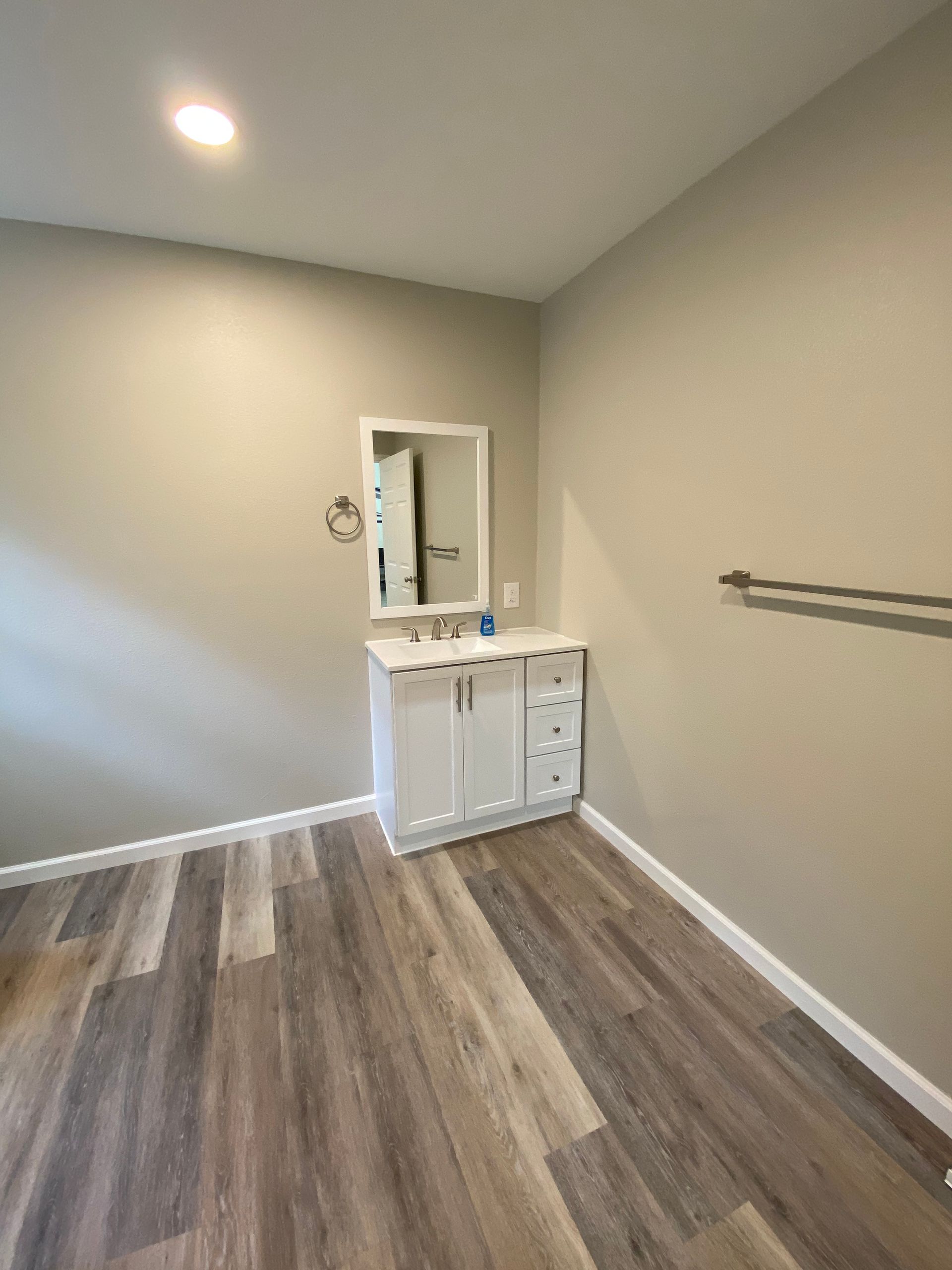 Bathroom with white vanity, mirror, towel bar. Light-colored walls and wood-look floor.