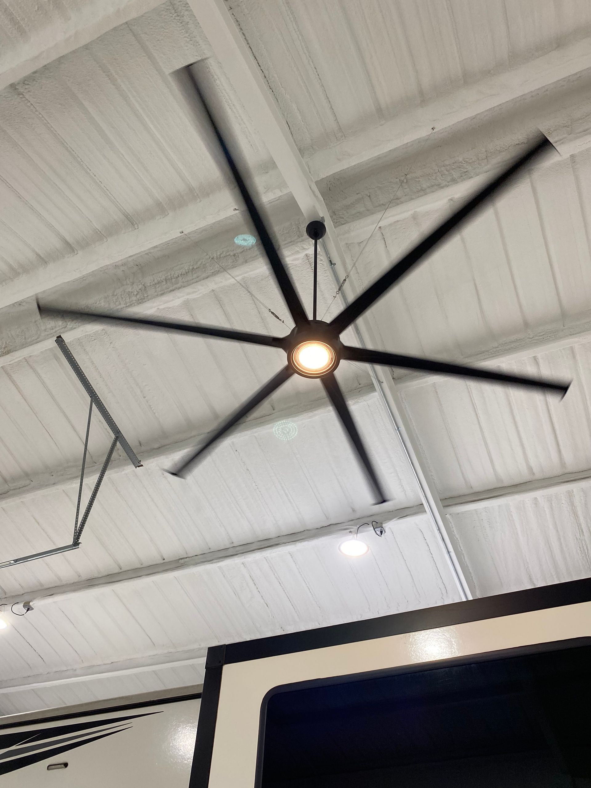 Black ceiling fan with six blades spinning, mounted on white ceiling.