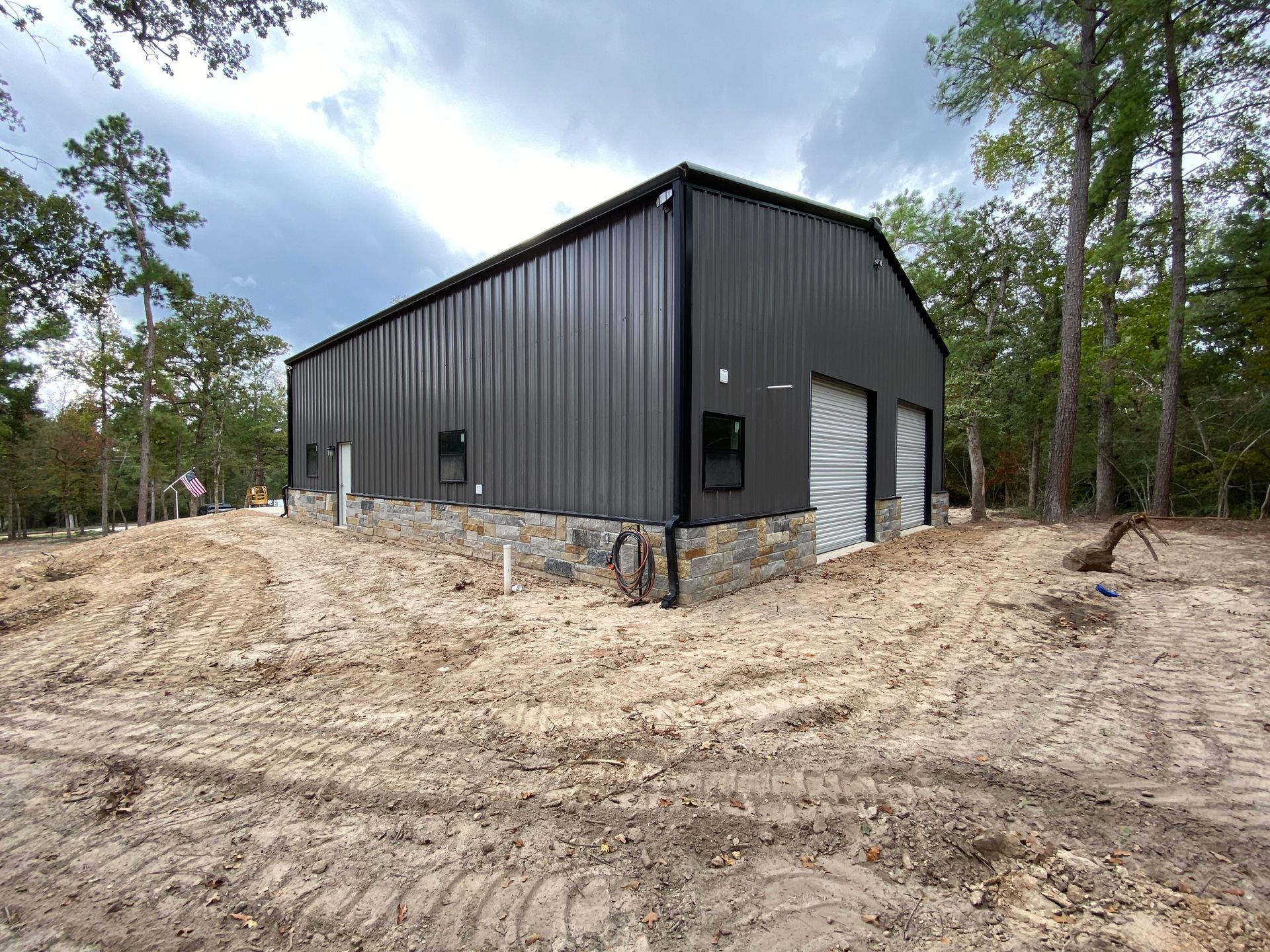 Dark gray metal building with stone base, set in a clearing.