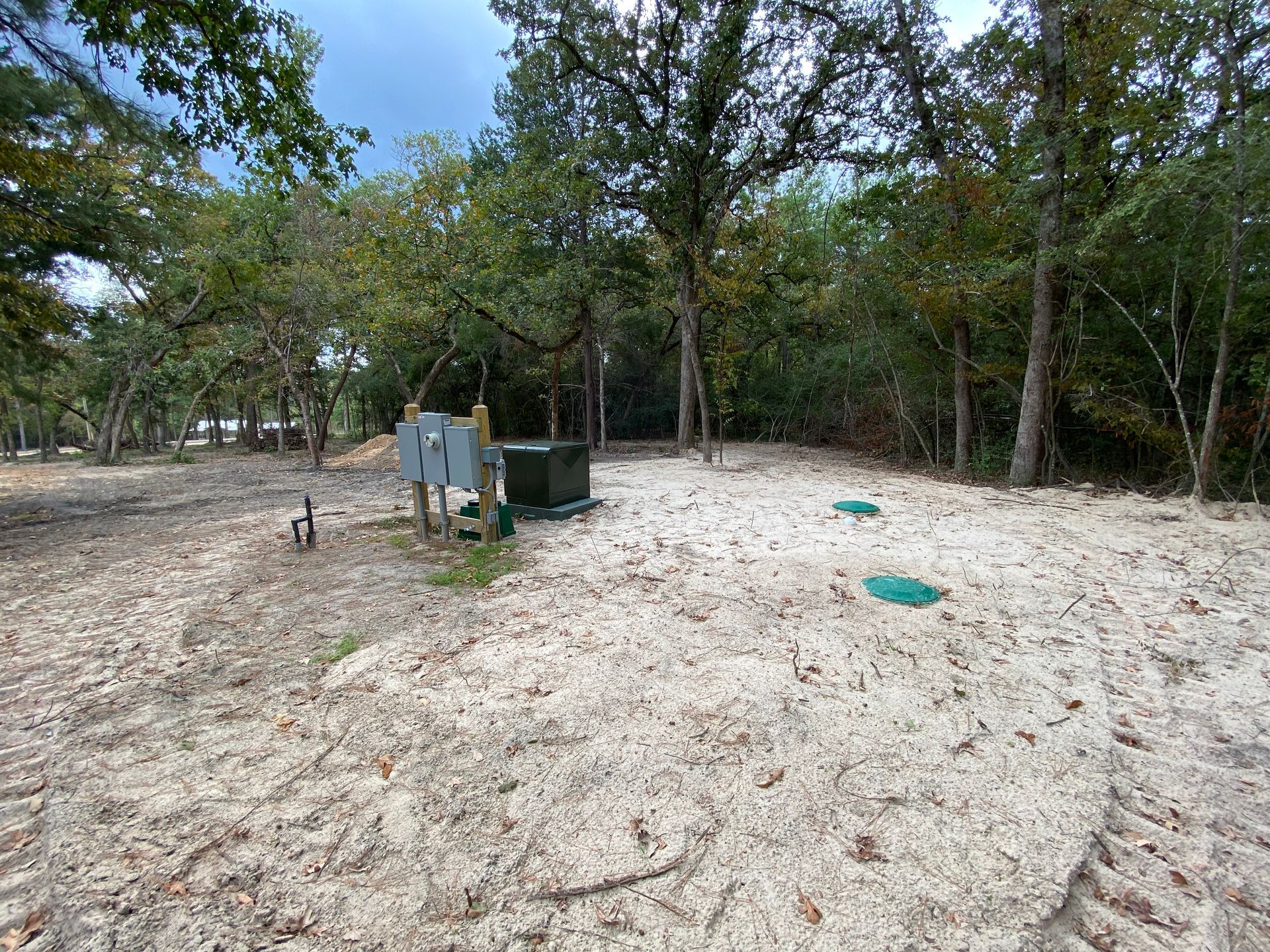 Sandy area with electrical box, septic tank lids, and trees in the background.