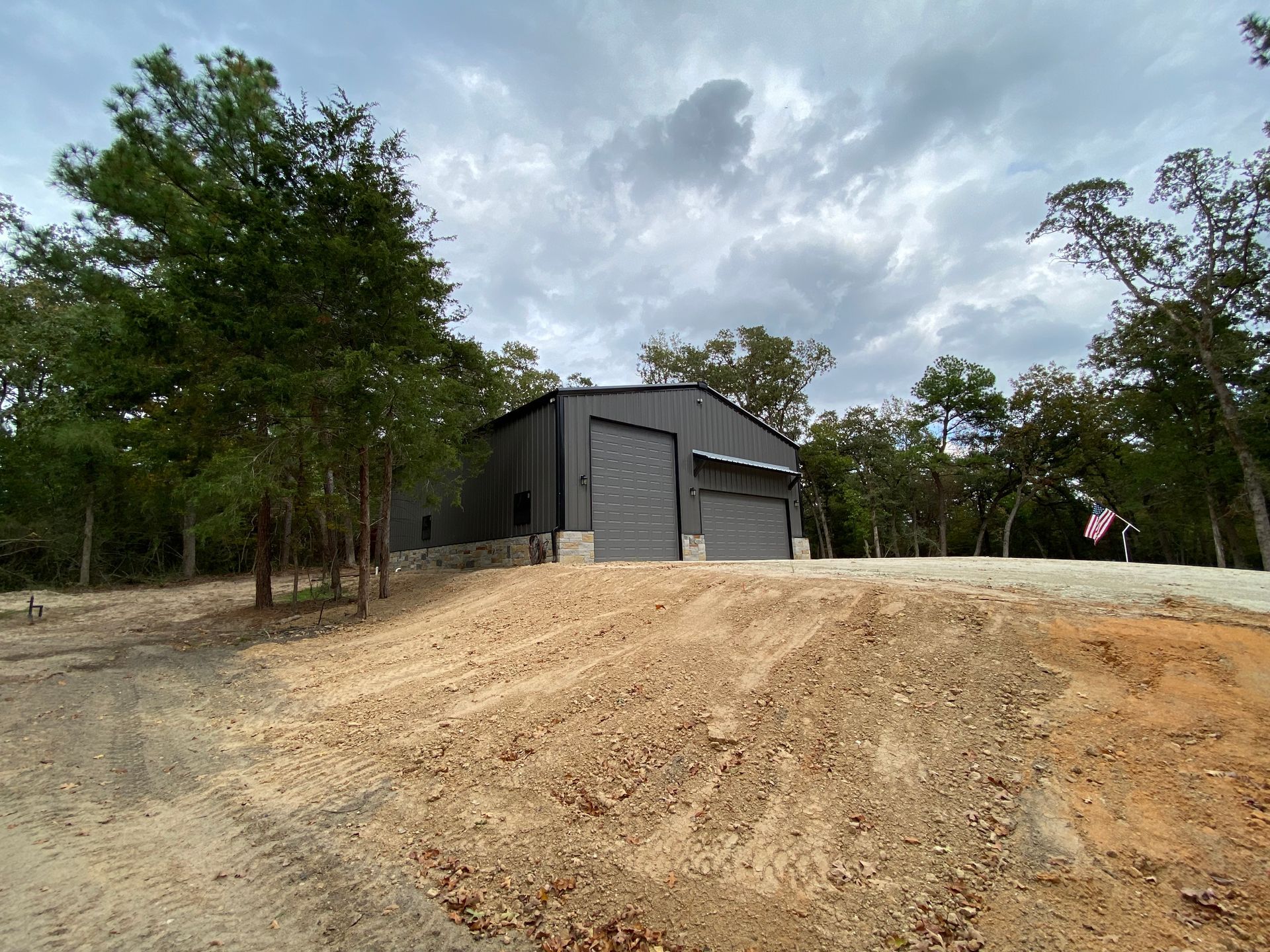 Dark grey metal building with garage doors, on a slight hill, cloudy sky.