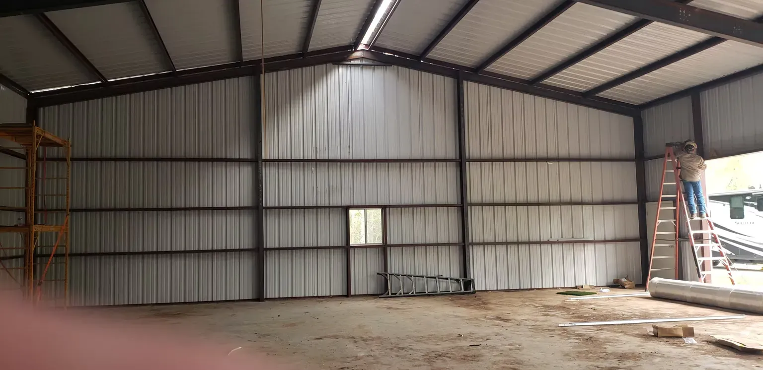 A man is standing on a ladder inside of a metal building.