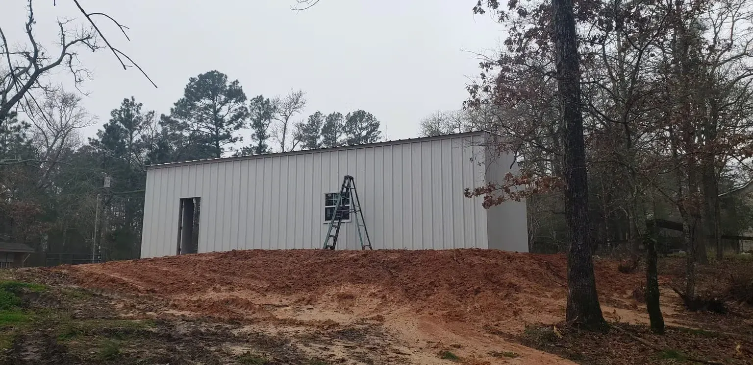 A white building is sitting on top of a dirt hill in the middle of a forest.