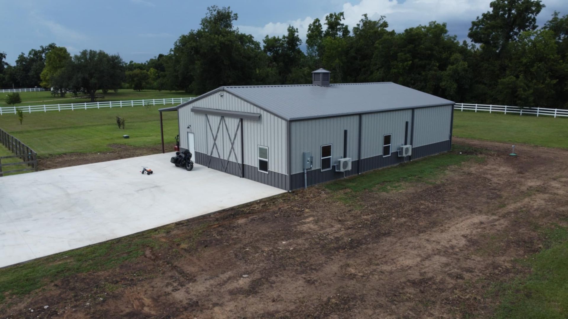 Large gray metal building with a concrete pad in a grassy field.