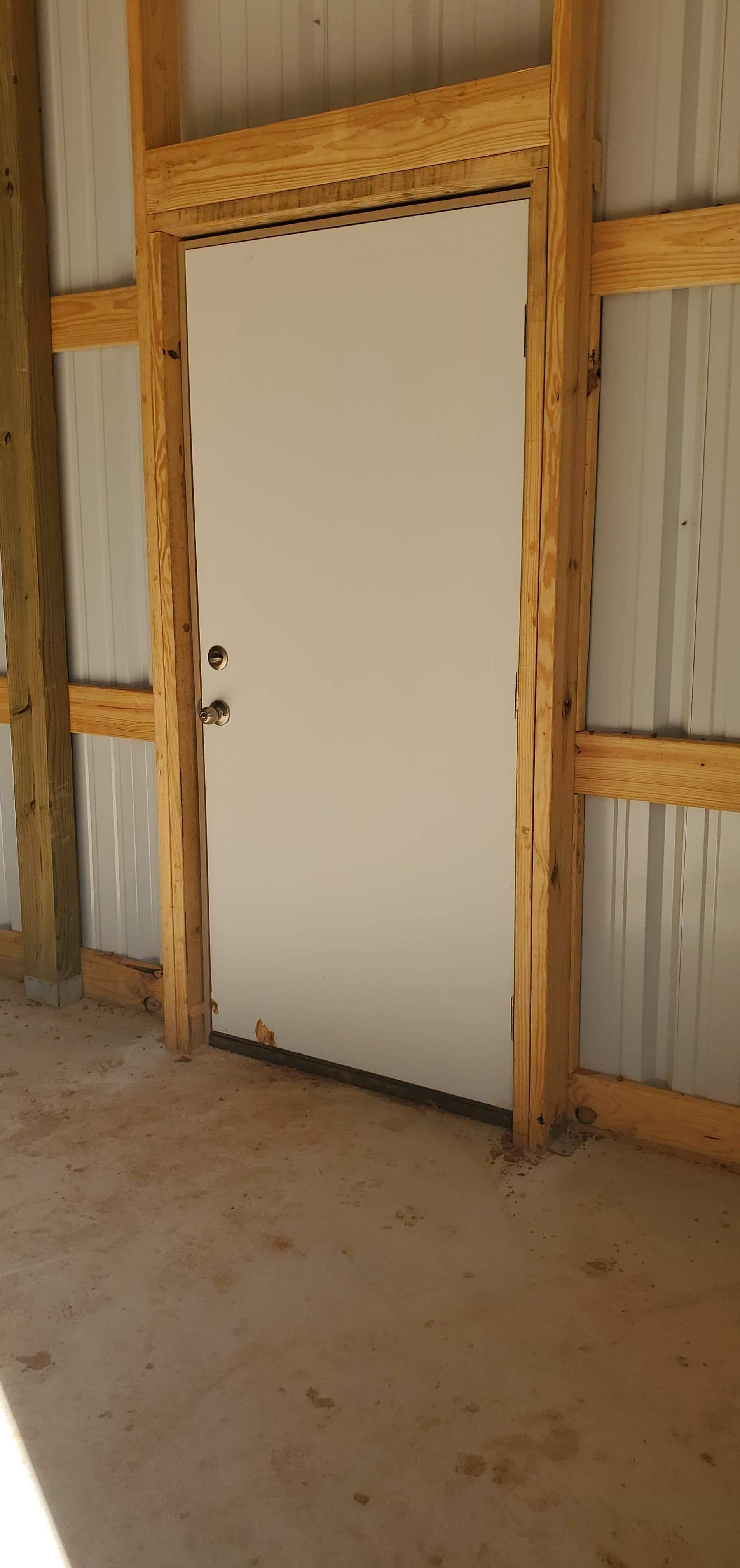 A white door framed by wooden beams, inside a building with a metal wall.