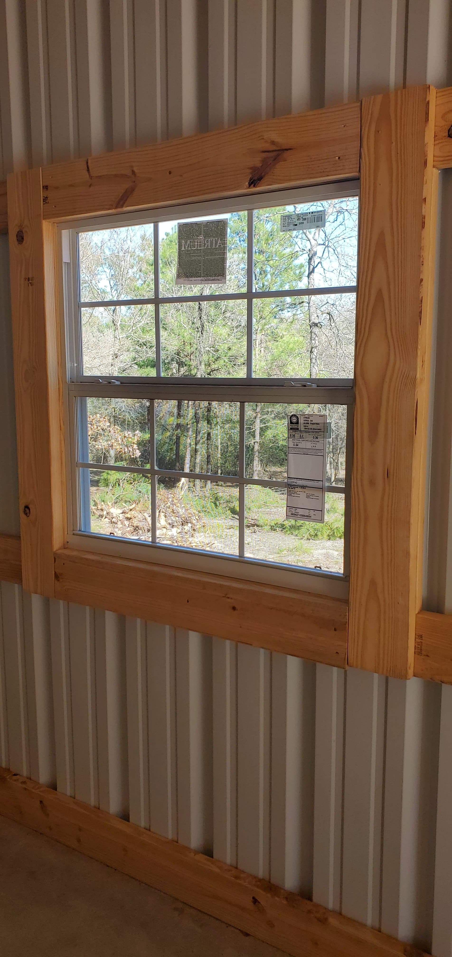 Window in a metal-walled building, with wooden framing. Outside view of trees.