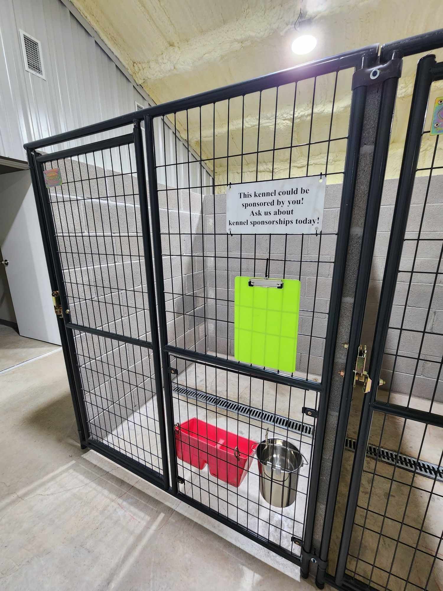 Dog kennels with metal gates. Red food bin and water bowl inside. Sign: 
