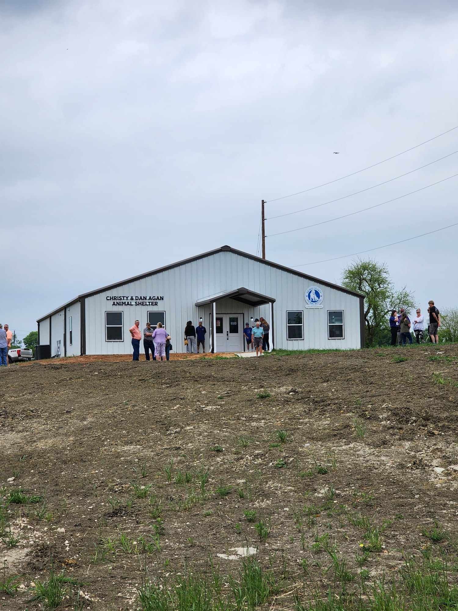 A white building with a dark roof and a group of people standing outside on a cloudy day.