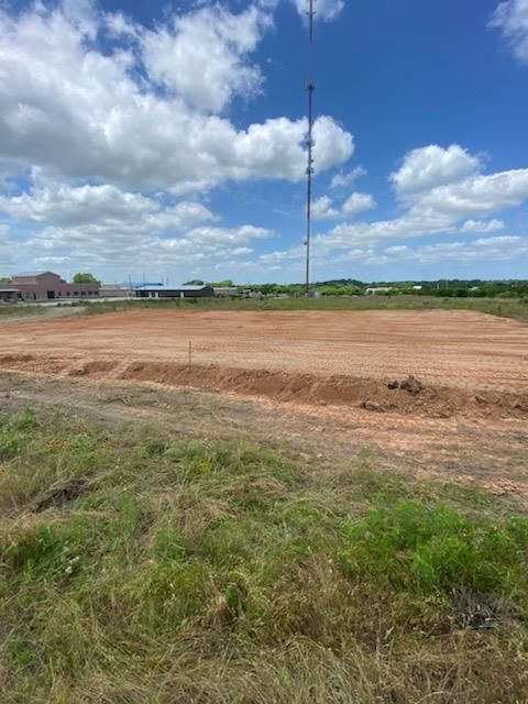 Cleared red dirt lot with a telecommunications tower under a partly cloudy sky.
