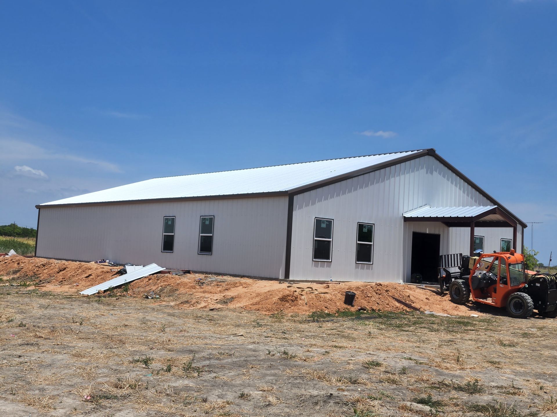 White metal building under construction; windows, brown trim, clear sky.
