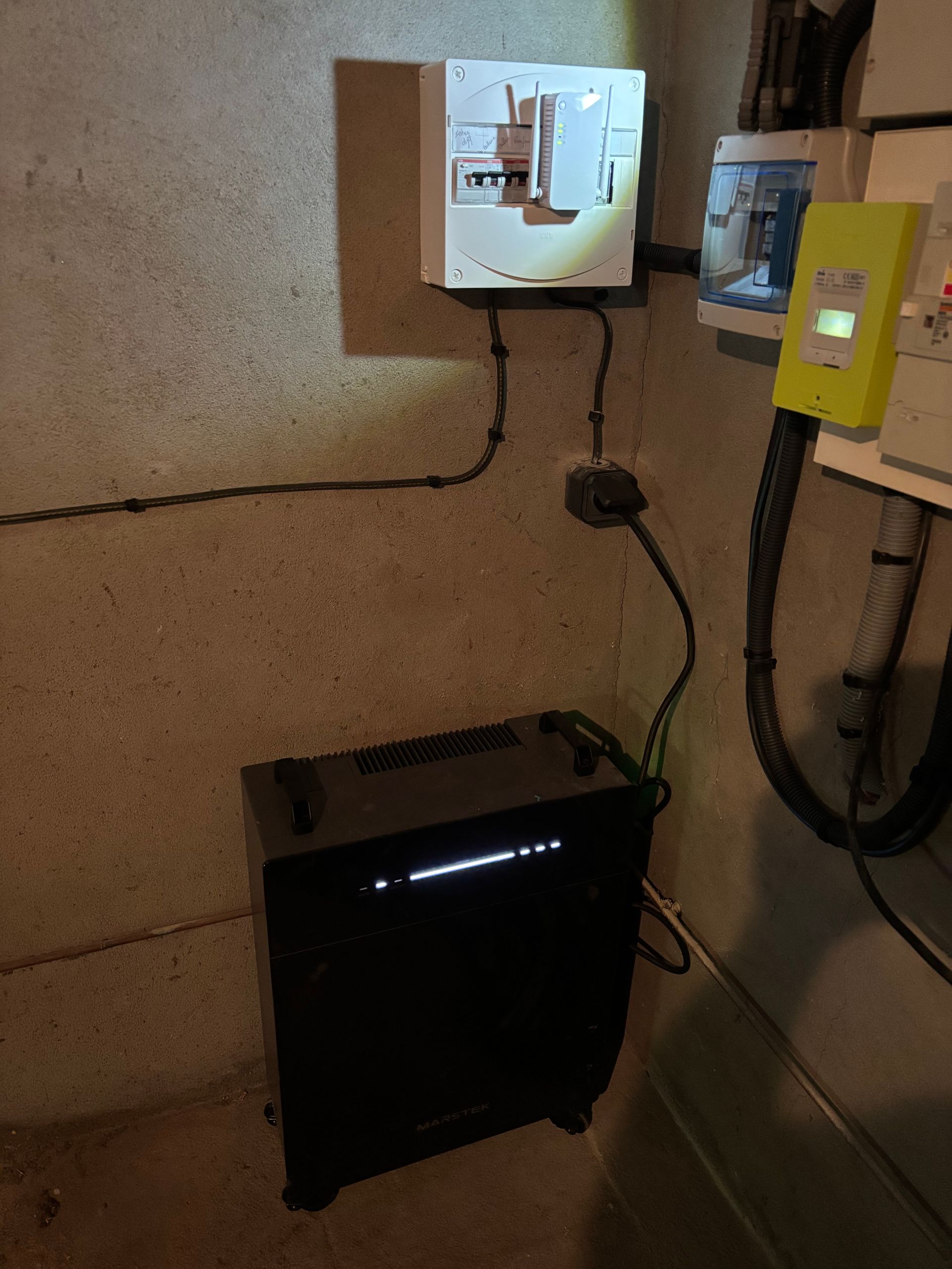 Boîte noire, panneau électrique et compteur jaune sur un mur en béton.