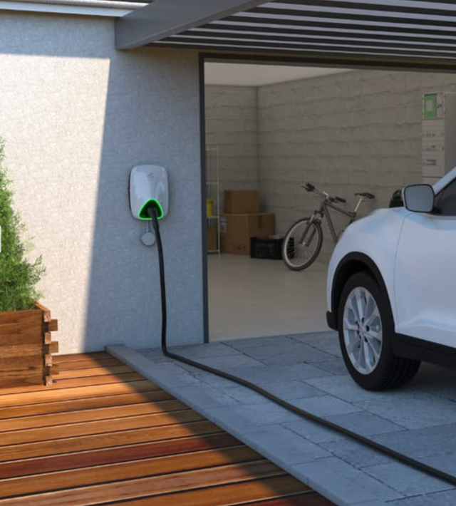 Chargeur EV et câble connectés à une voiture blanche garée dans un garage avec un vélo et des boîtes.