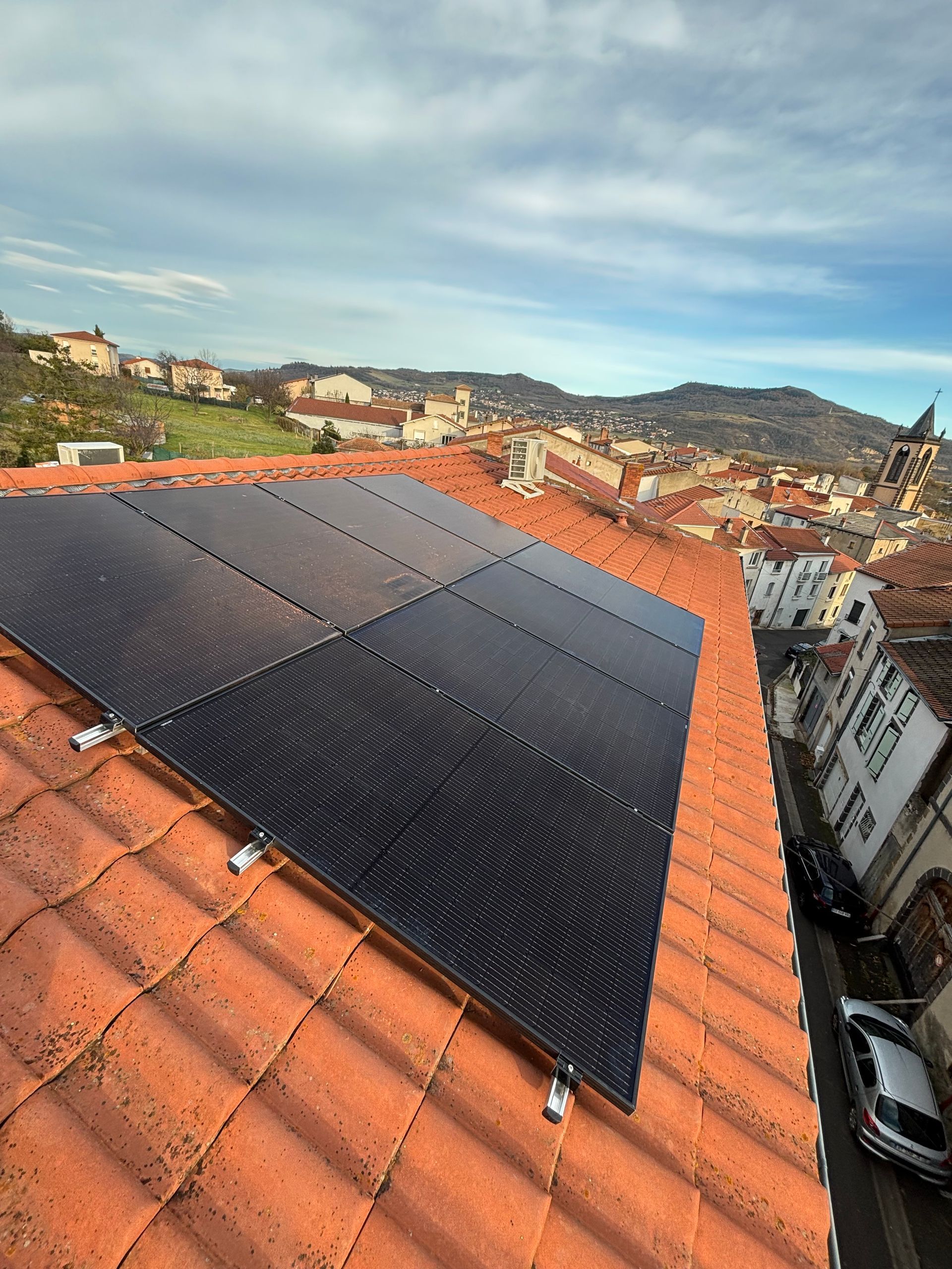 Panneaux solaires sur un toit de tuiles rouges avec un arrière-plan urbain et un ciel bleu.