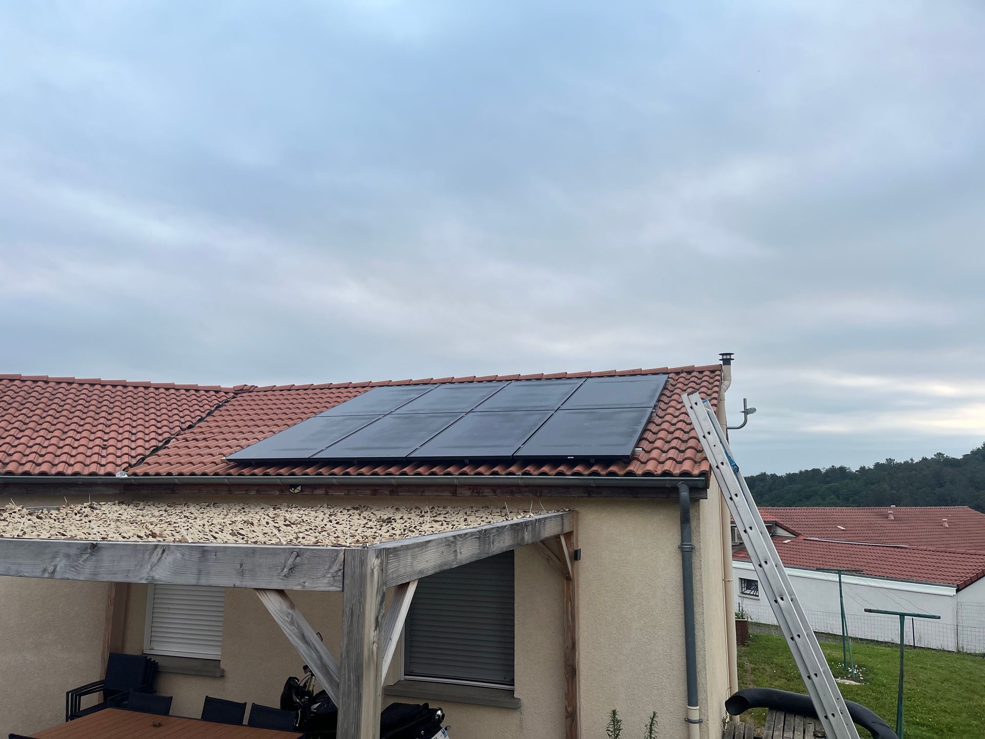 Panneaux solaires installés sur le toit en tuiles rouges d'une maison sous un ciel nuageux.