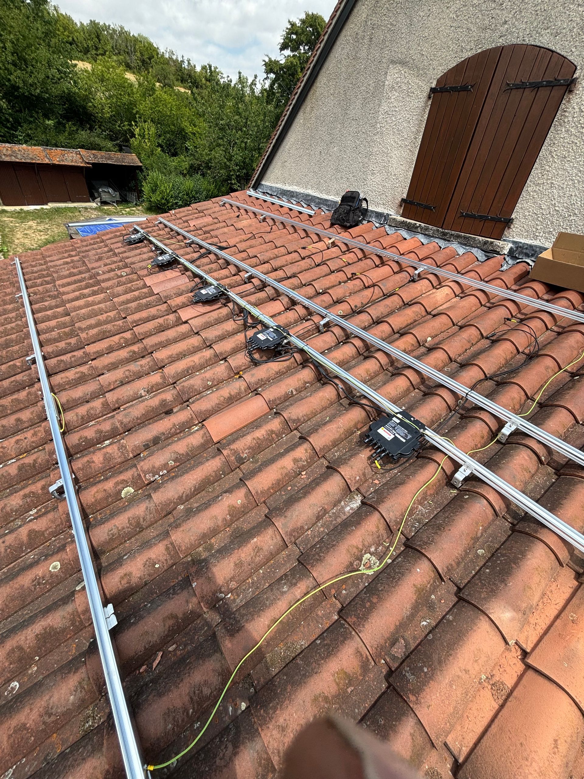 Matériel de montage de panneaux solaires installé sur un toit en tuiles rouges.