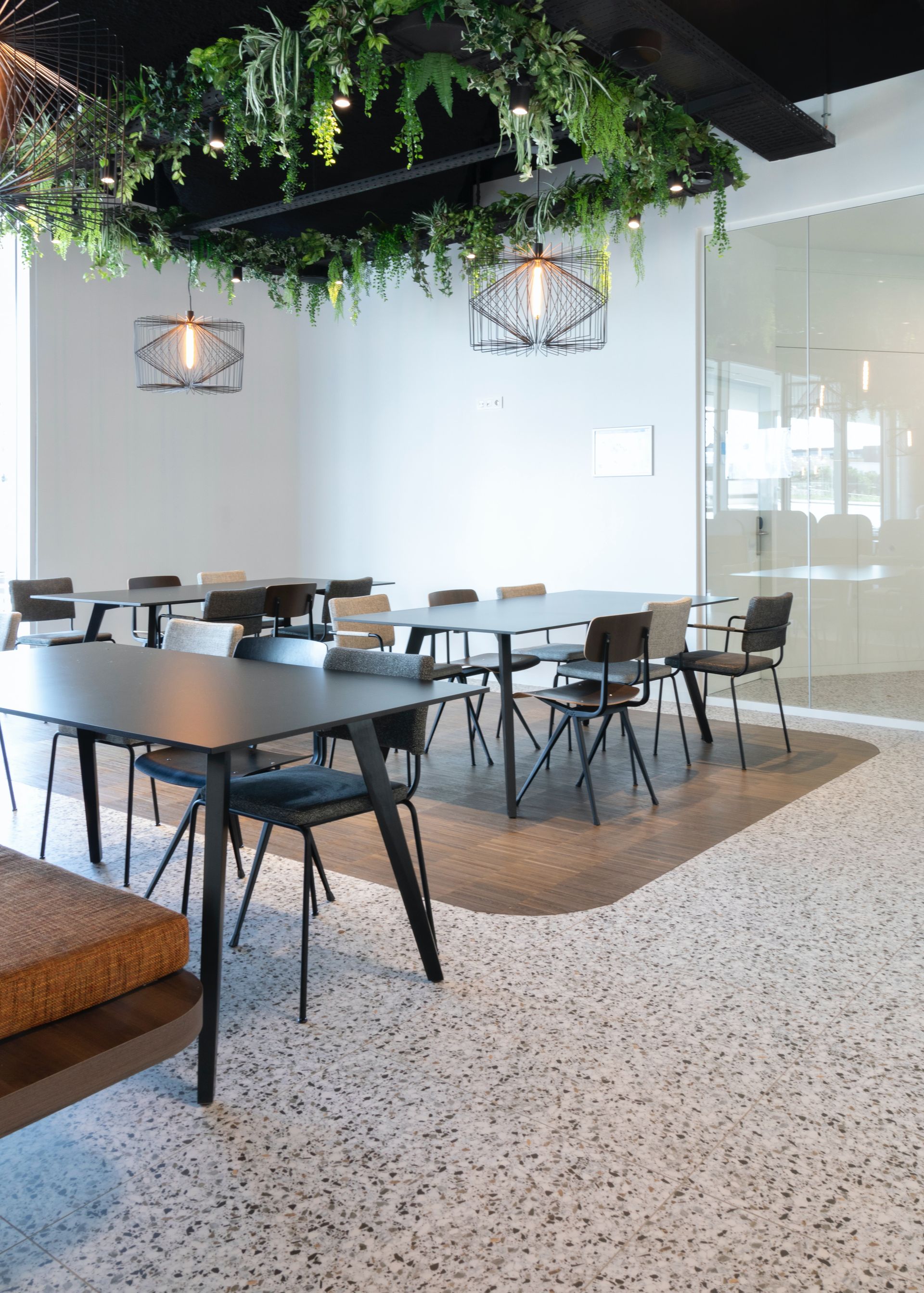 Een kantine, vergaderruimte met tafels en stoelen en planten die aan het plafond hangen
