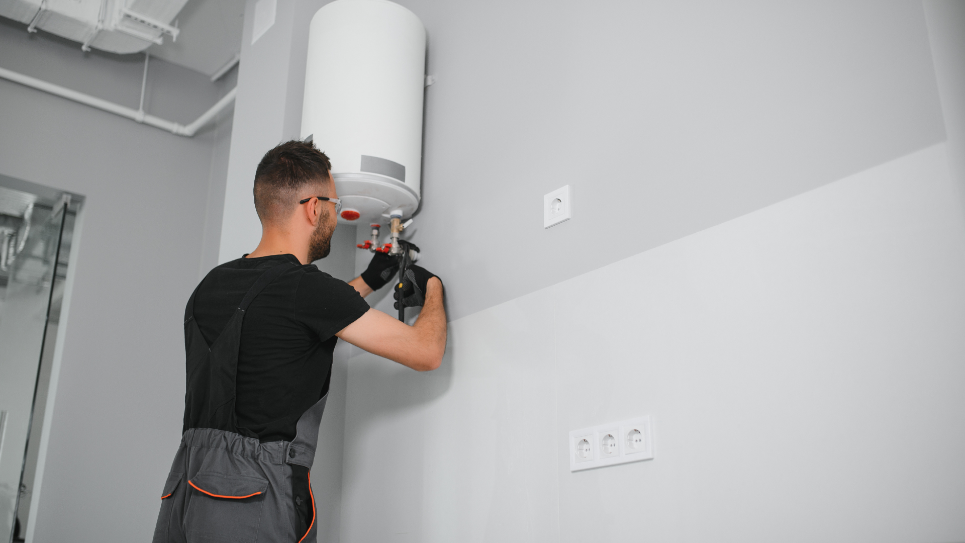 Plumber installing a water heater in a gray room.