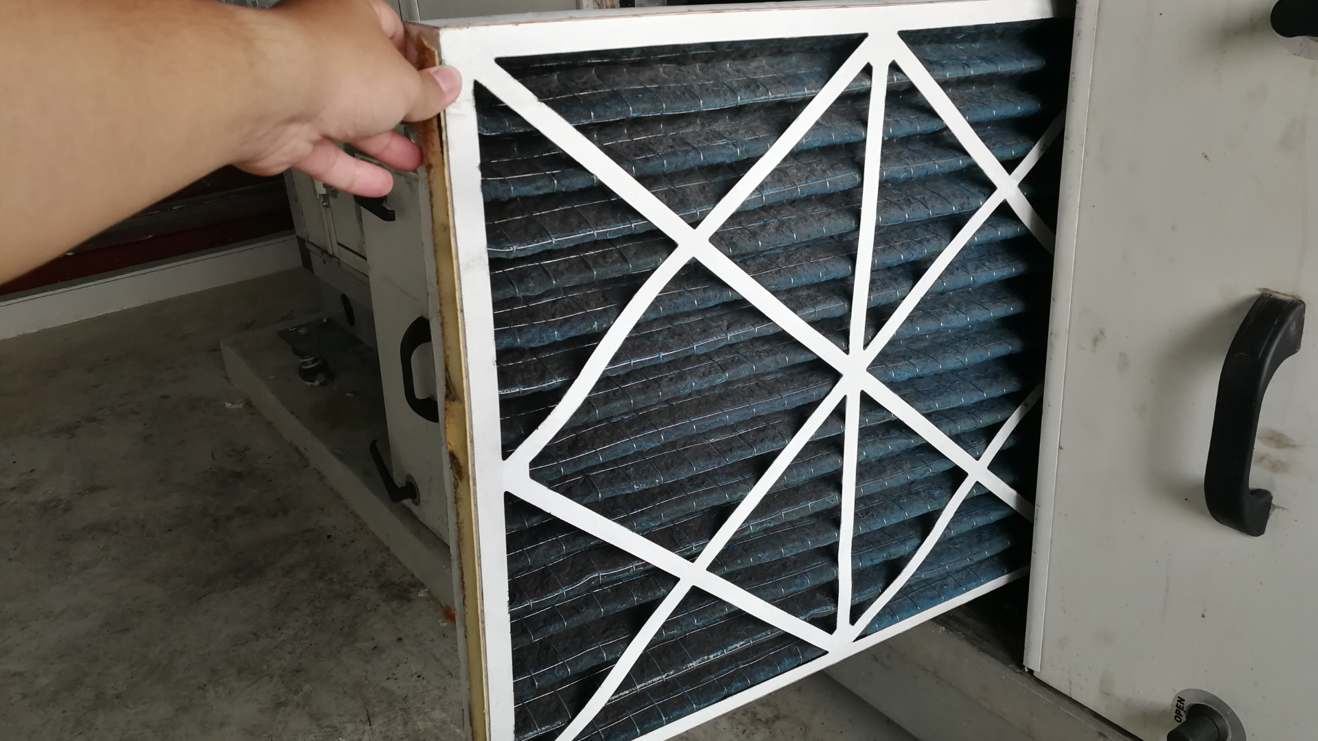 Hand removing a dirty, pleated HVAC filter from a metal housing.