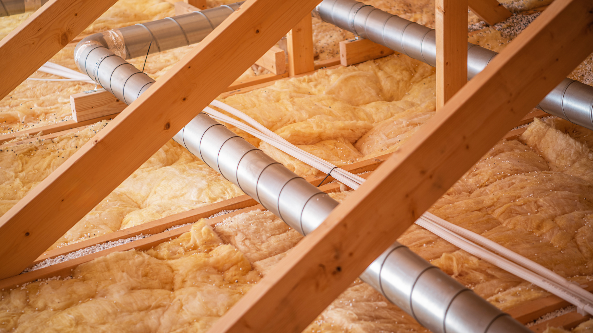 Attic with wooden beams, air ducts, and yellow insulation.