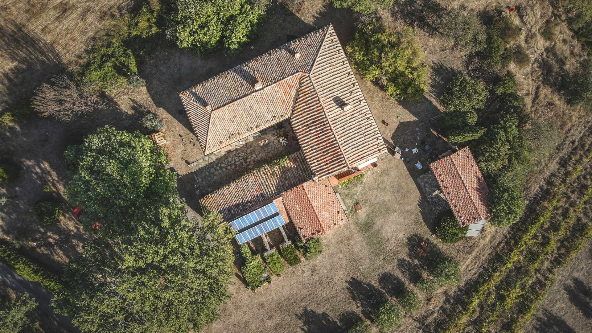 Aerial view of a rustic building with a red-tiled roof, surrounded by trees and dry vegetation.