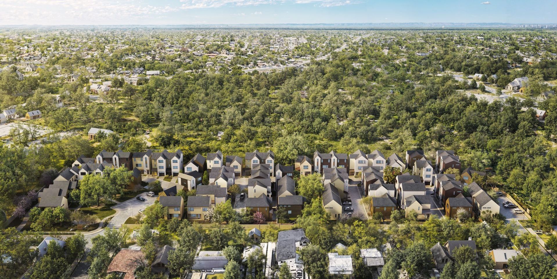 Aerial view of a residential neighborhood surrounded by dense green trees. Homes have various colors and styles.