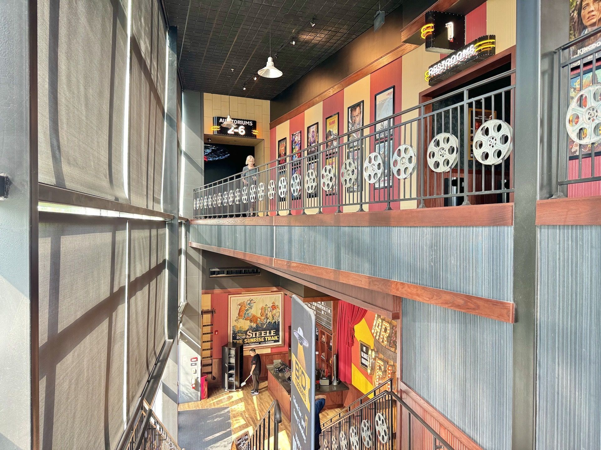 Two-story movie-themed hallway with film reel decorations, framed movie posters, and a lower level exhibition.