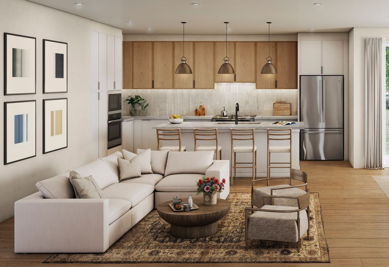 Open-concept living space: white sectional sofa, kitchen island with stools, light wood cabinets, and art on the walls.