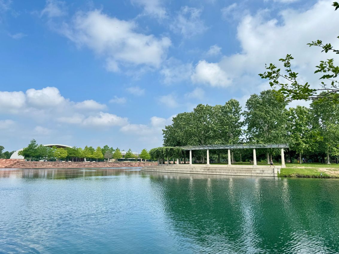 Blue lake with a pergola, trees, and a partly cloudy sky.