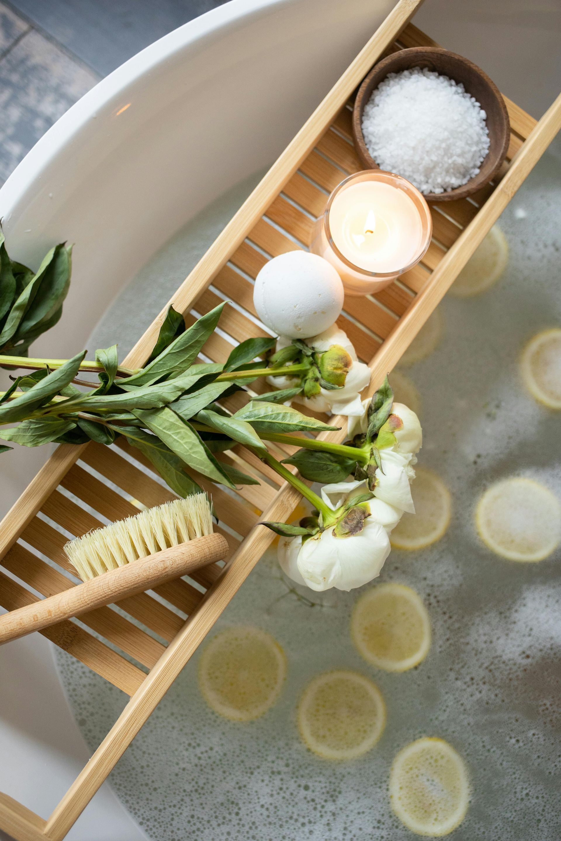 Bathtub setup with bath salts, candle, lemon slices, flowers, and bath brush.