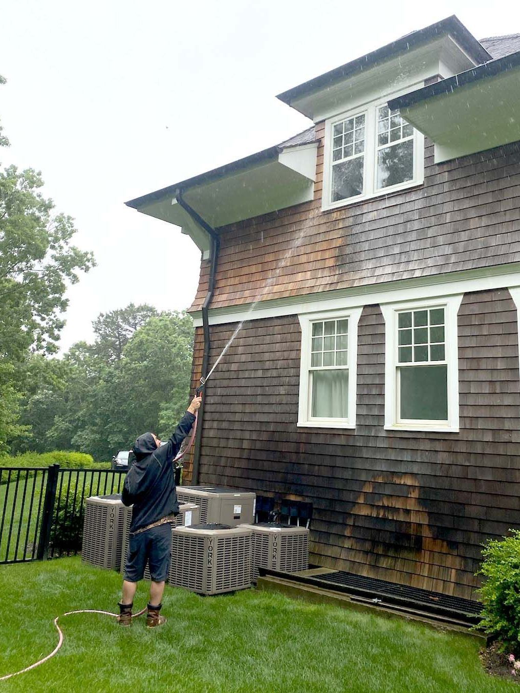 Technician soft washing green algae from vinyl siding on a Suffolk County home